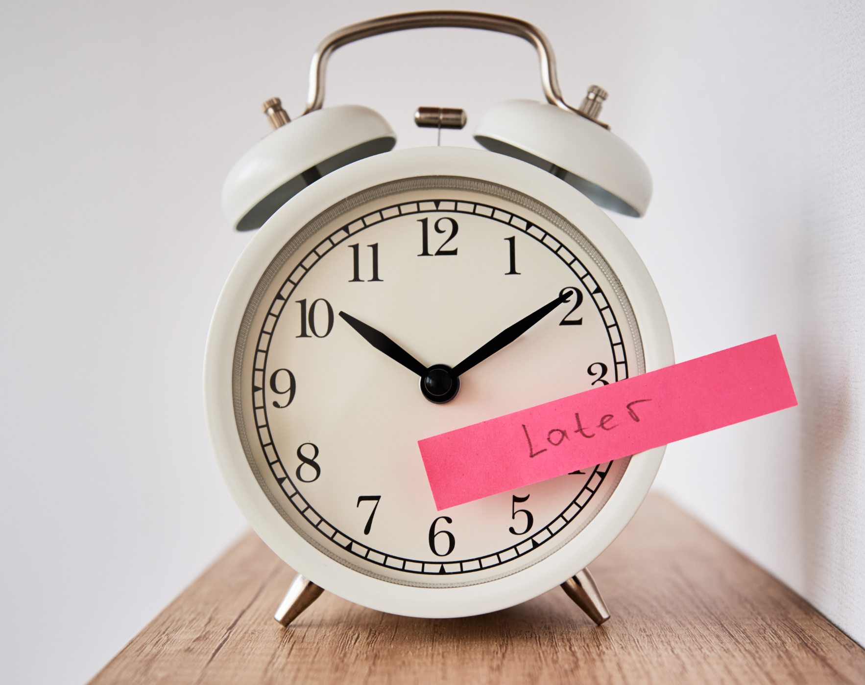 White alarm clock with a sticky note that says “Later,” symbolizing the MS biological clock by Alene Brennan and the cost of delaying healthy habits.